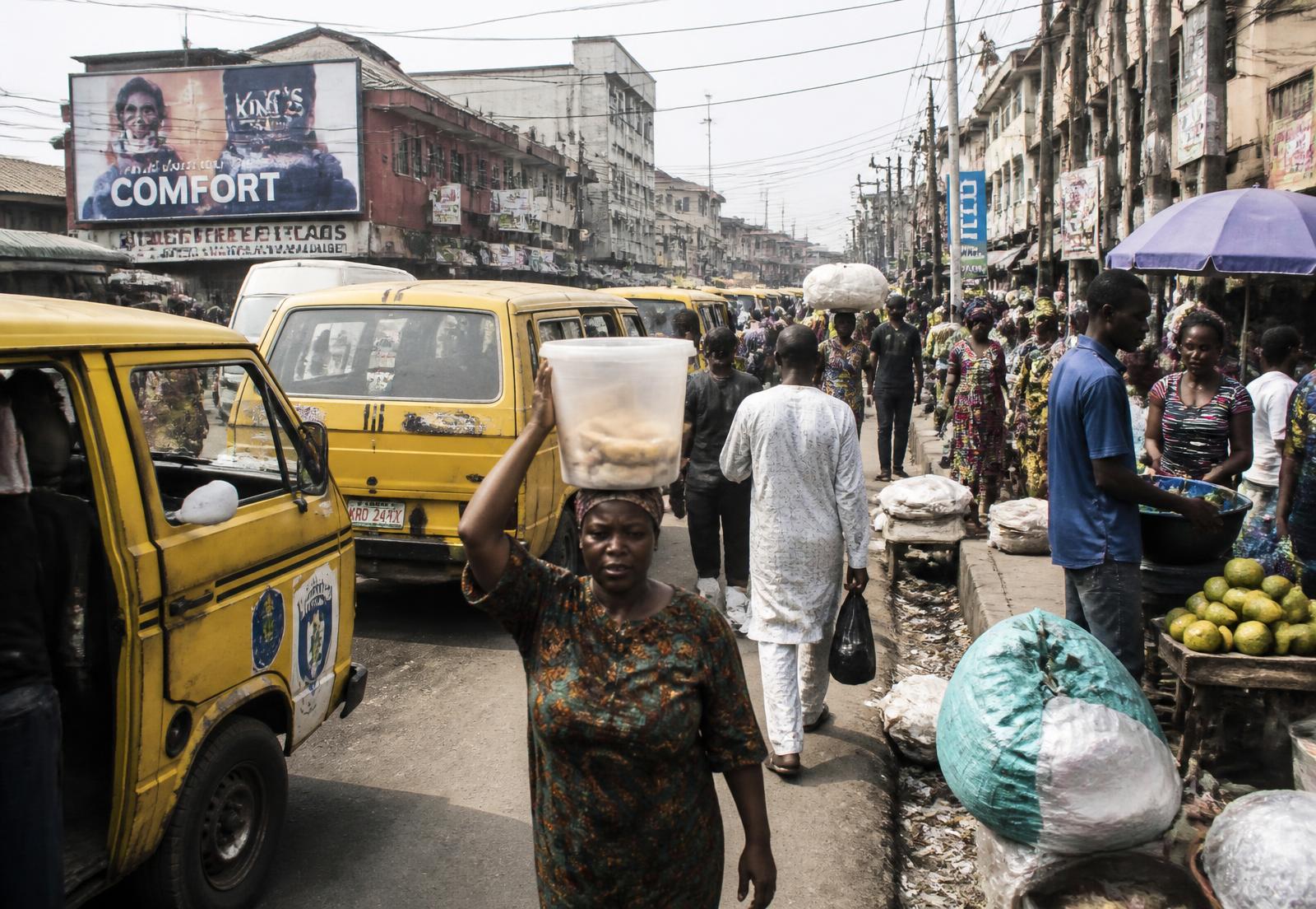A crowded Lagos market street with yellow danfo buses