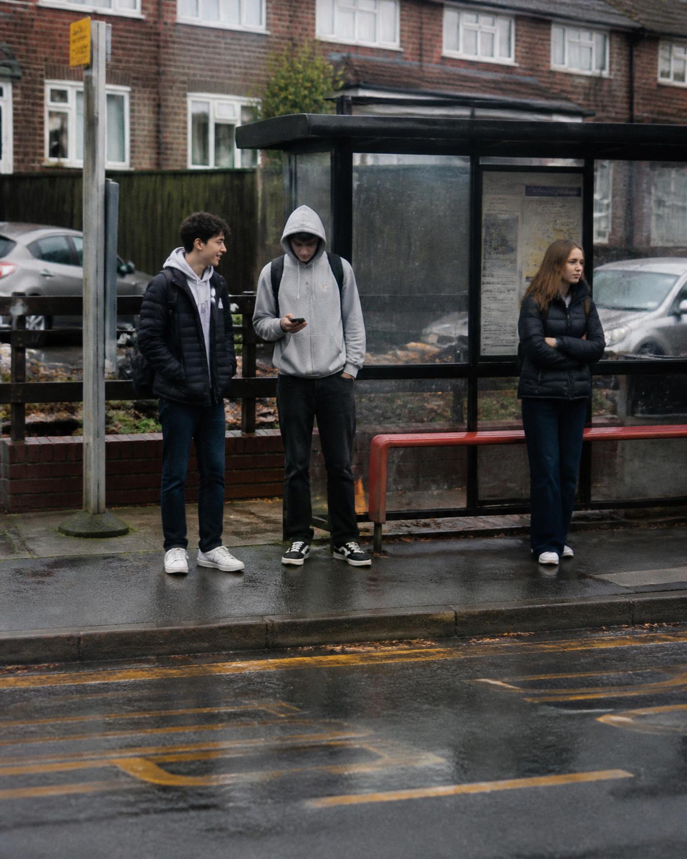 Three friends waiting at a bus stop on a rainy British street